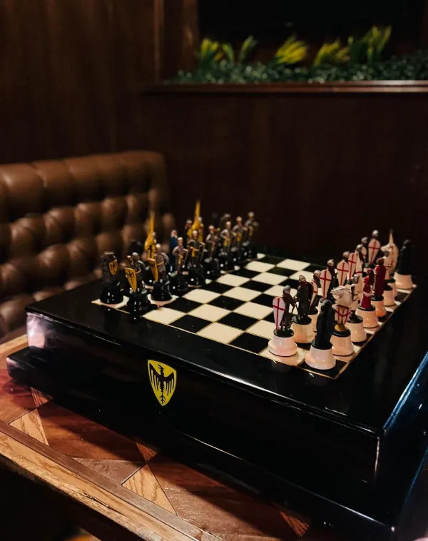 Tablero de ajedrez con piezas de caballeros medievales, junto a un sillón capitonado de piel