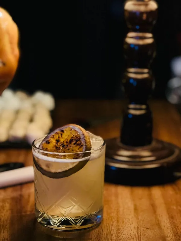 Cóctel con hielo y una rodaja de cítrico tostada, en un vaso labrado