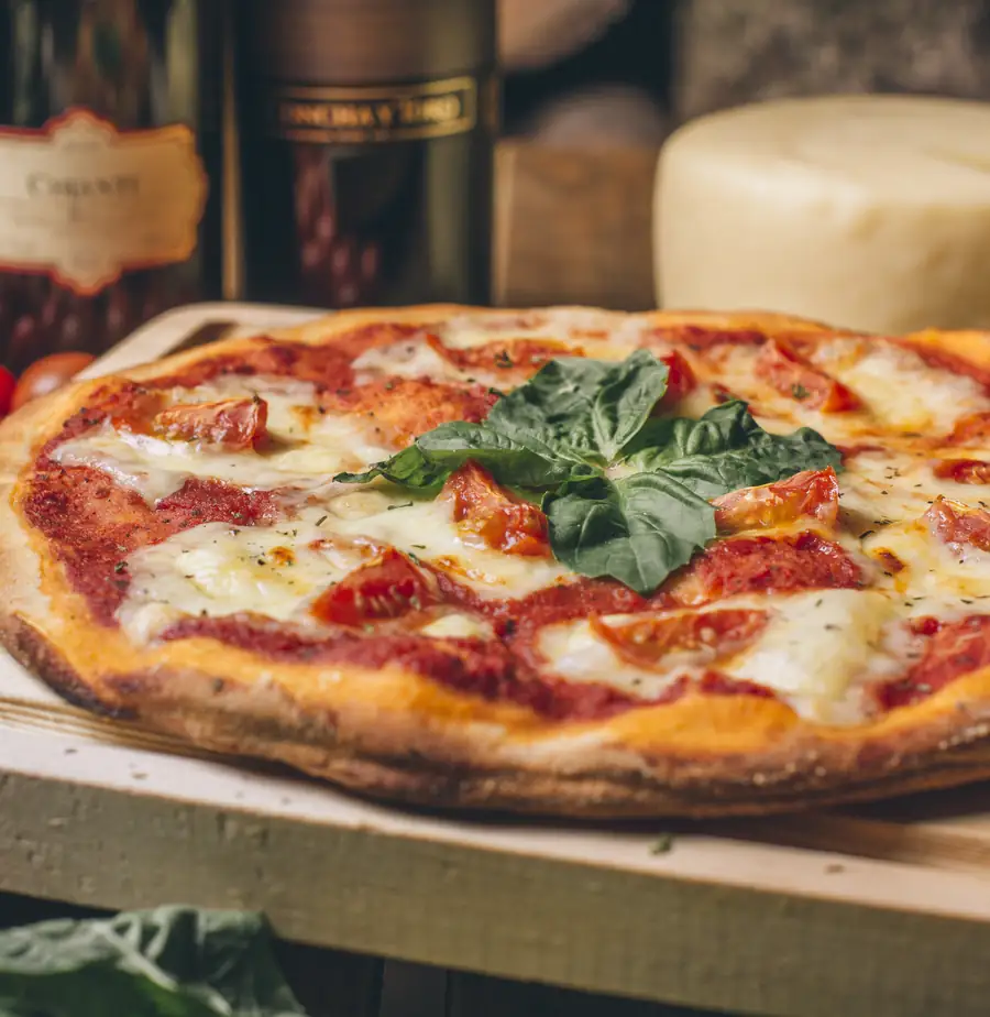 Pizza margarita recién horneada con albahaca, junto a quesos y vino